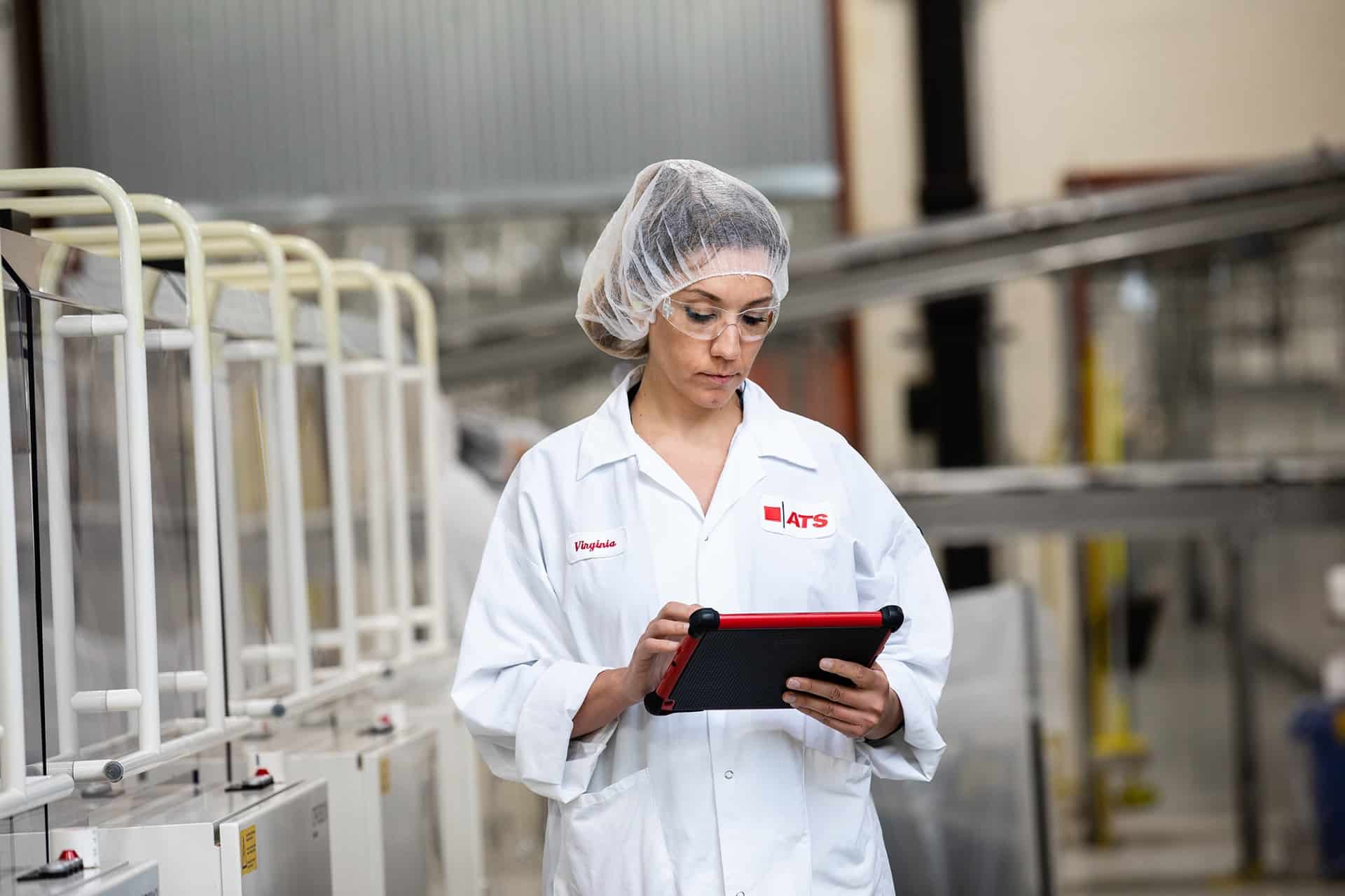 Woman in hairnet holding tablet in plant.