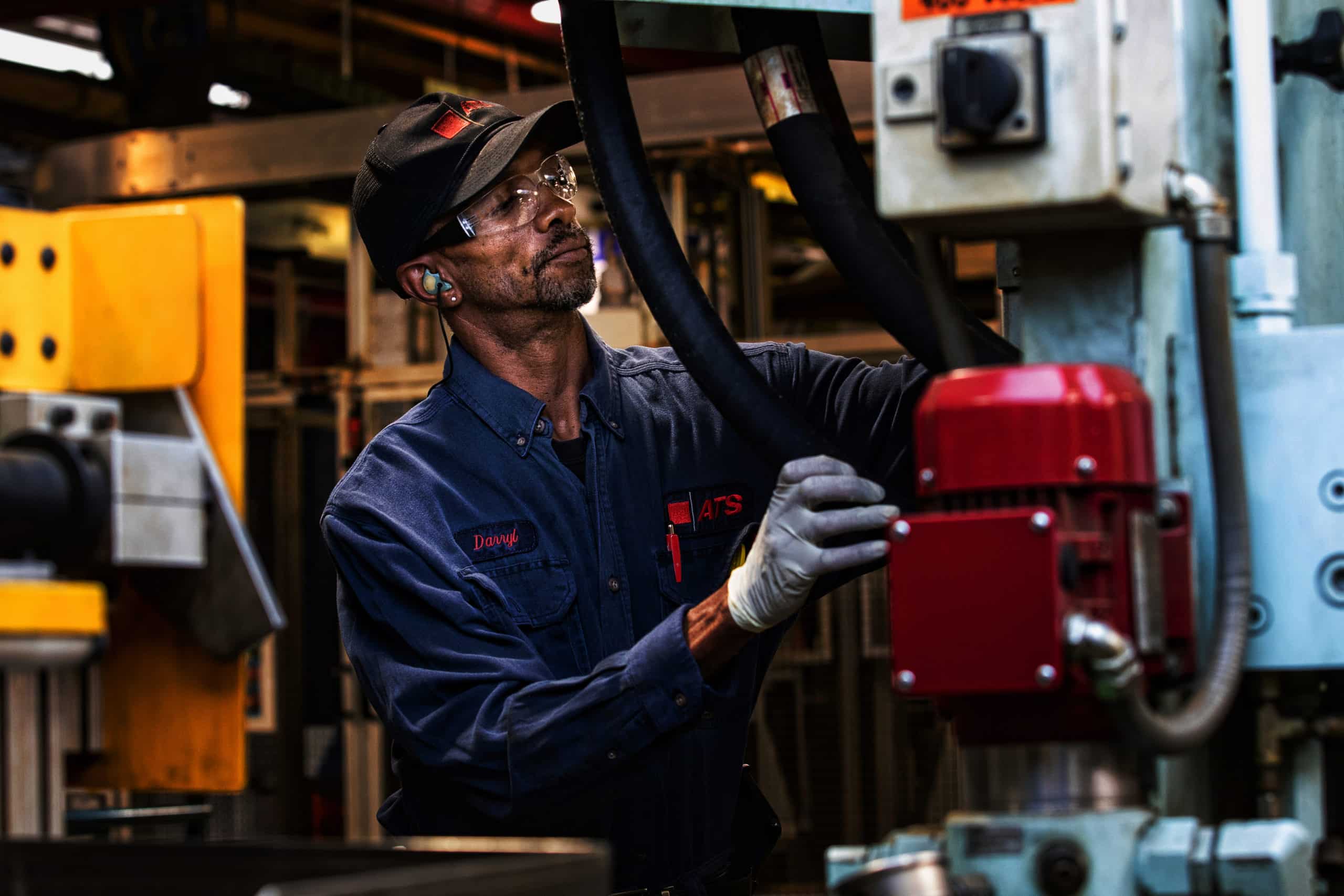 Man with hat and protective glasses adjusting machinery.