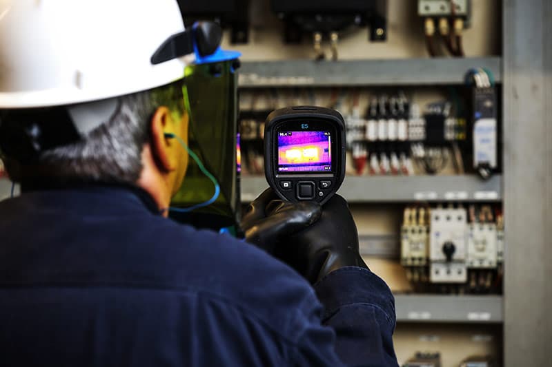 Man pointing thermographic imaging device at equipment.
