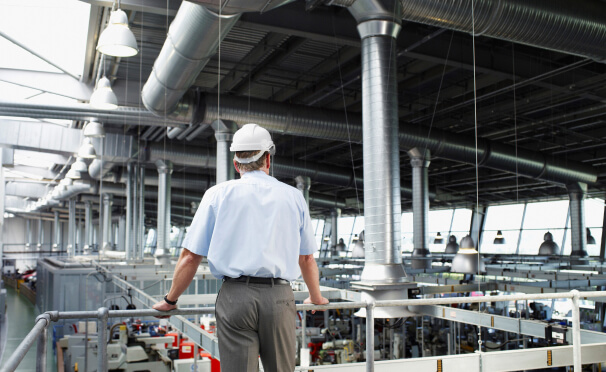 Man wearing dress clothes and hard hat looking across factory