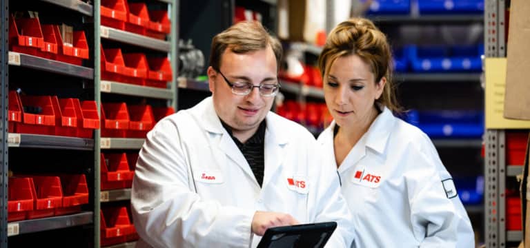 Man and woman in ATS uniforms view tablet in factory