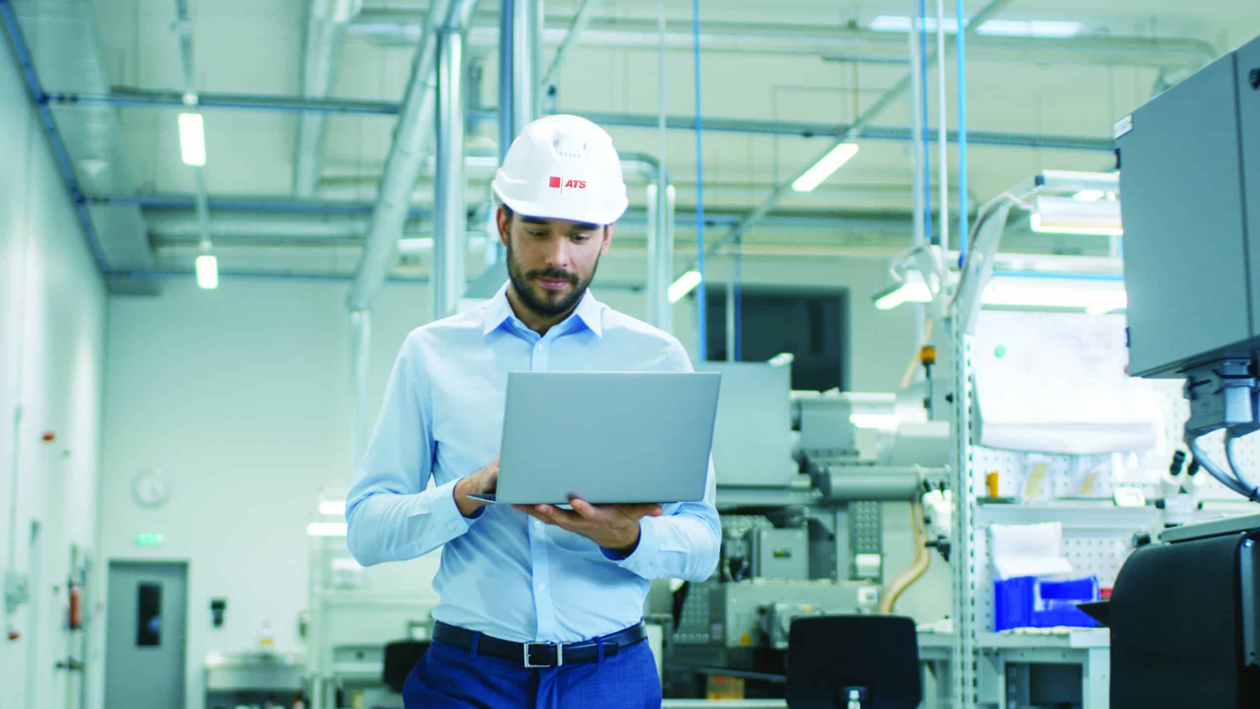 Man walking in factory while working on a laptop.