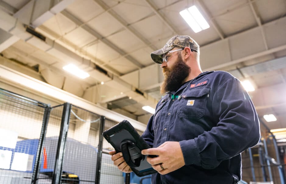 Man in a camo hat holding an iPad looking to the left in a factory