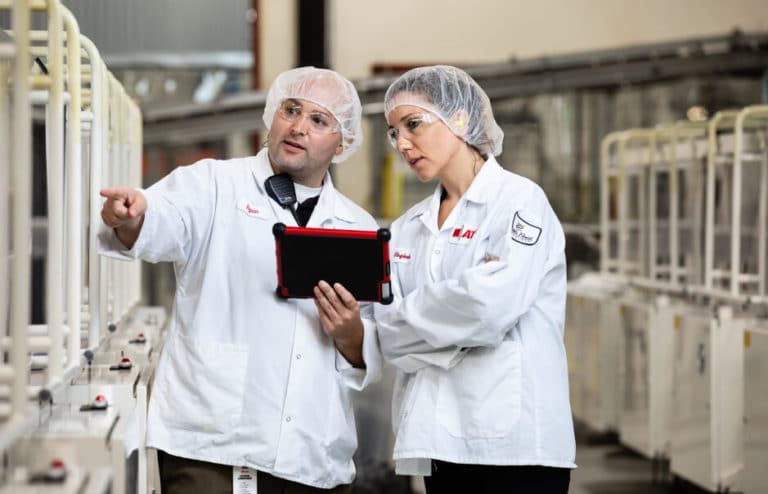 A man and a woman in hairnets interacting with machine and an iPad
