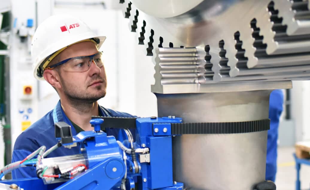 Man wearing ATS hard hat and safety glasses closely looking at machinery