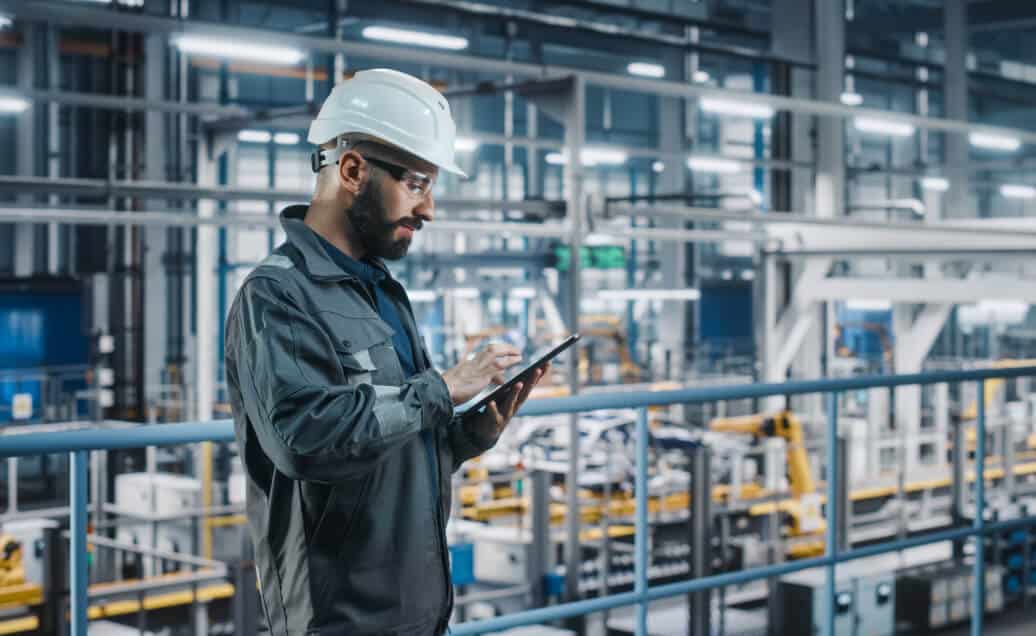 Middle aged man in safety gear looking at an iPad inside a factory