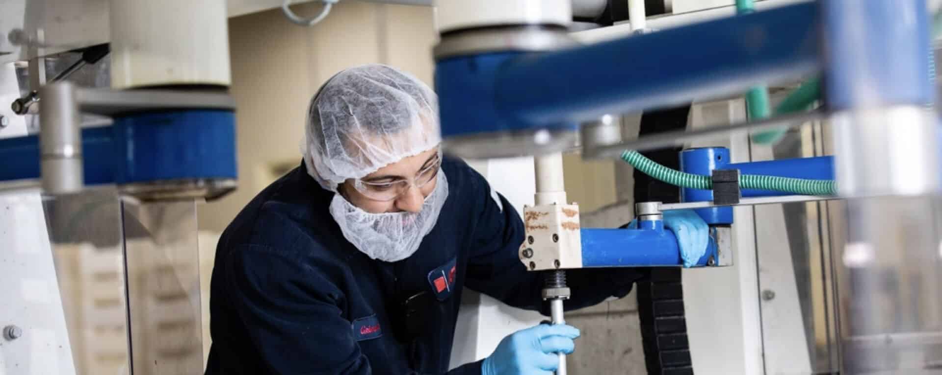 Gloved man wearing two hairnets operates machinery