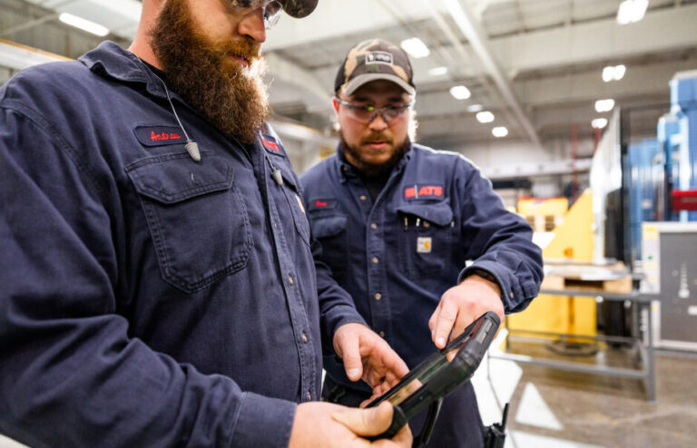 Two men in ATS uniforms viewing tablet in factory