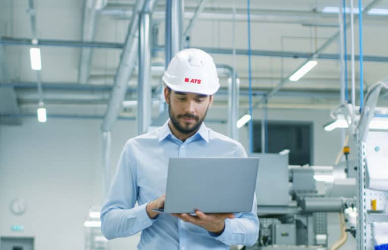 Man in ATS hard hat holding and viewing laptop