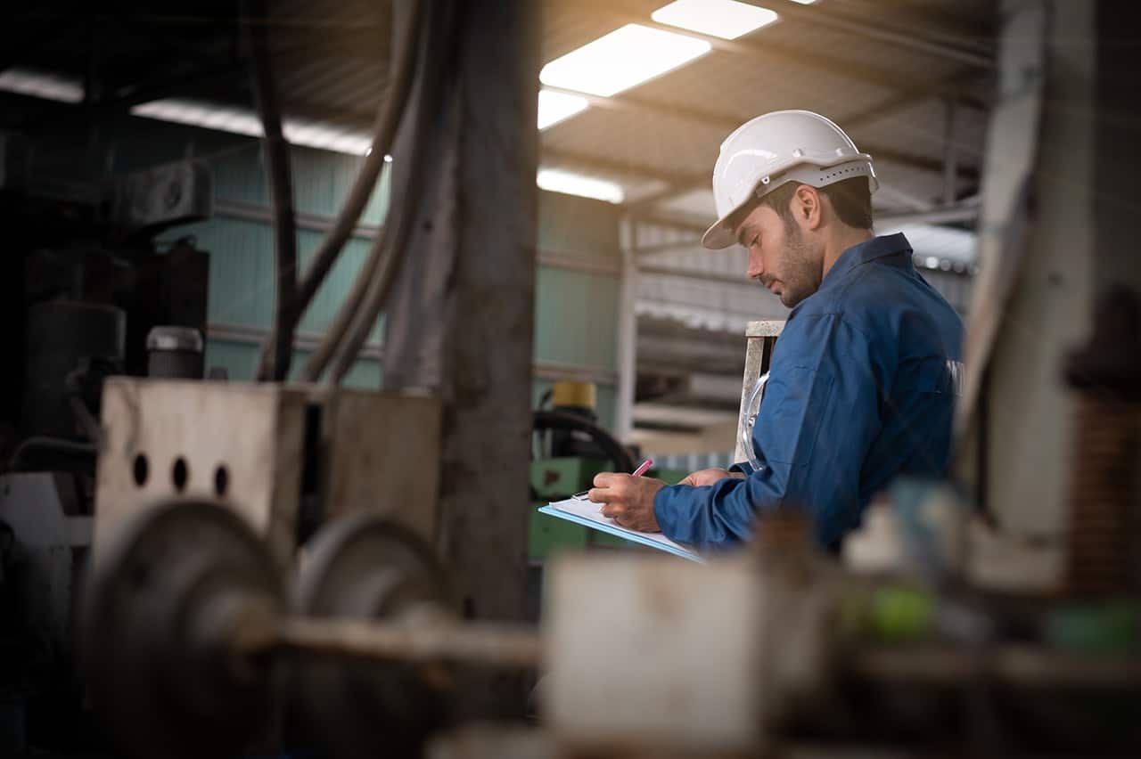 Man in hard hat writing on clipboard.