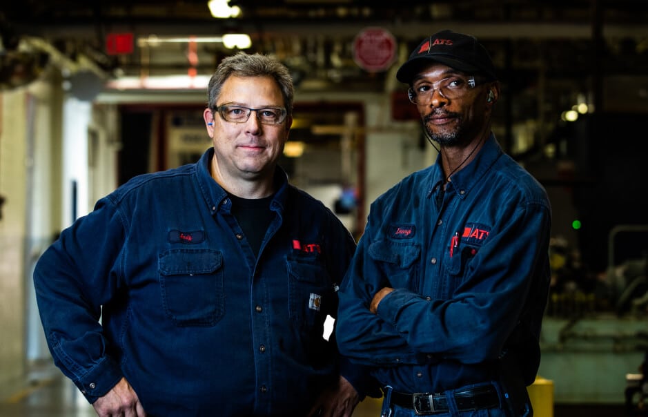 Two men wearing ATS jumpsuits looking at the camera