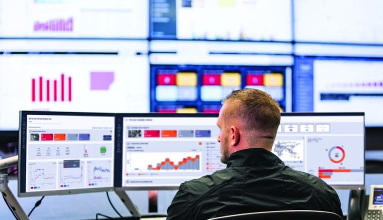 Rear view of a man working on multiple desktop screens