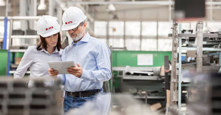 Man and woman in ATS hard hats view tablet in factory