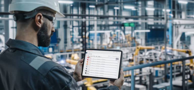 Car factory engineer in work uniform using a tablet showing machine data.
