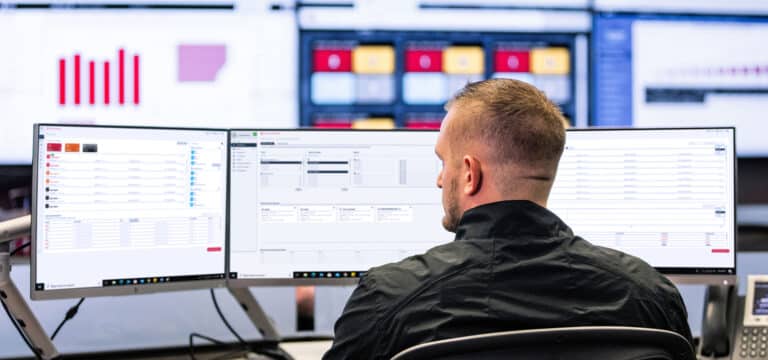 Rear view of a man working on multiple desktop screens.