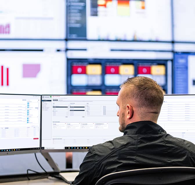 Rear view of a man working on multiple desktop screens.