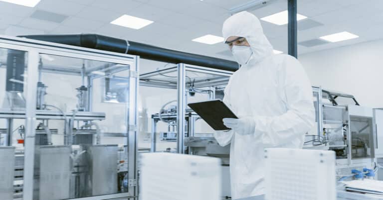 Scientist Using Digital Tablet Computer and wearing Protective Suit walks through Manufacturing Laboratory.
