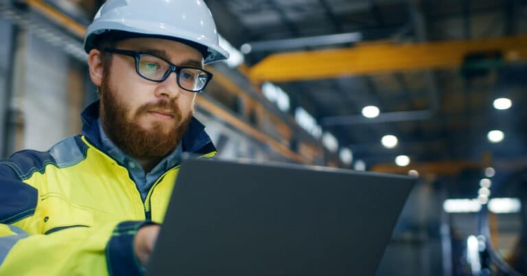 Industrial Engineer in Hard Hat Wearing Safety Jacket Uses Touchscreen Laptop.