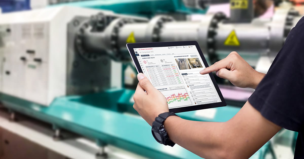 Man standing next to machine holding an iPad looking at sensor alerts dashboard.