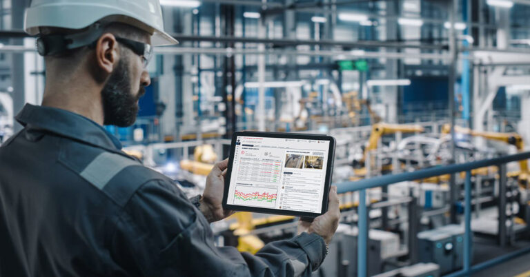 Car factory engineer in work uniform using a tablet showing machine data.