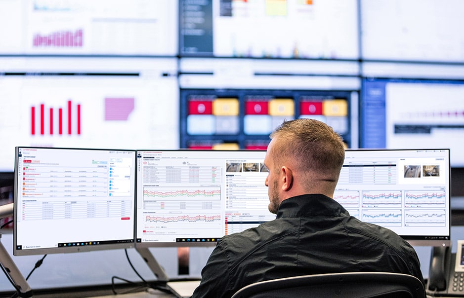 Rear view of a man working on multiple desktop screens.