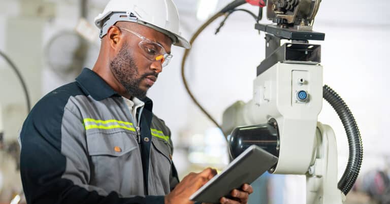 African mechanical engineer repairing robotic welding machine in factory.