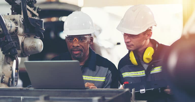 Two male technicians using a computer to control an automated robotic arm in the factory.