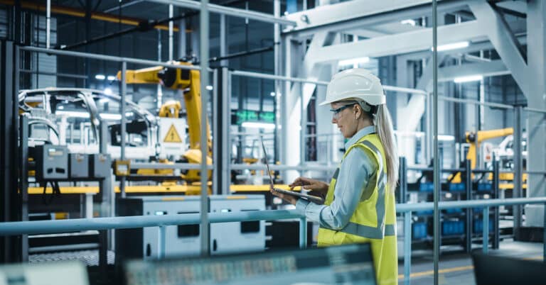 Woman overlooking manufacturing floor while utilizing technology