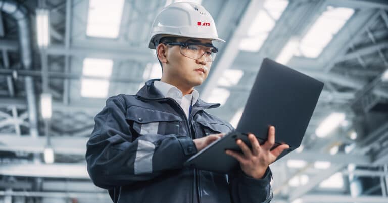 ATS reliability engineer reviewing data on laptop in manufacturing facility.