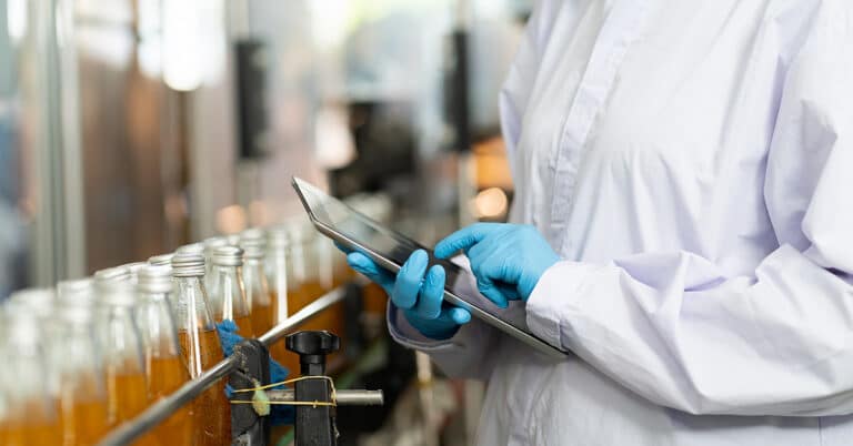 Hands of worker with digital tablet checking quality control of product on the conveyor belt in a beverage factory.