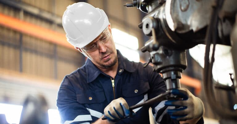 Male technician wearing safety glasses and helmet operating heavy-duty machinery in the lathing factory.