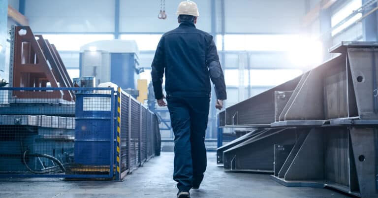 Factory worker in a hard hat walking through industrial facilities.