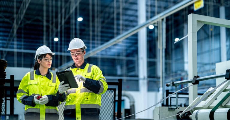 Male and female engineer in PPE controlling a production system in a factory using technology.