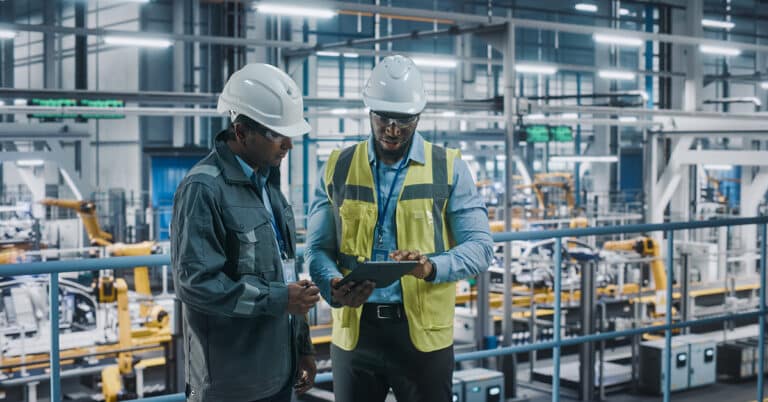Multiethnic manager and African American engineer using tablet in manufacturing setting.