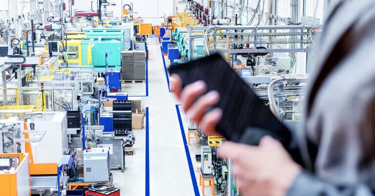 Woman holding a tablet computer standing on top of a balcony overlooking a manufacturing floor.