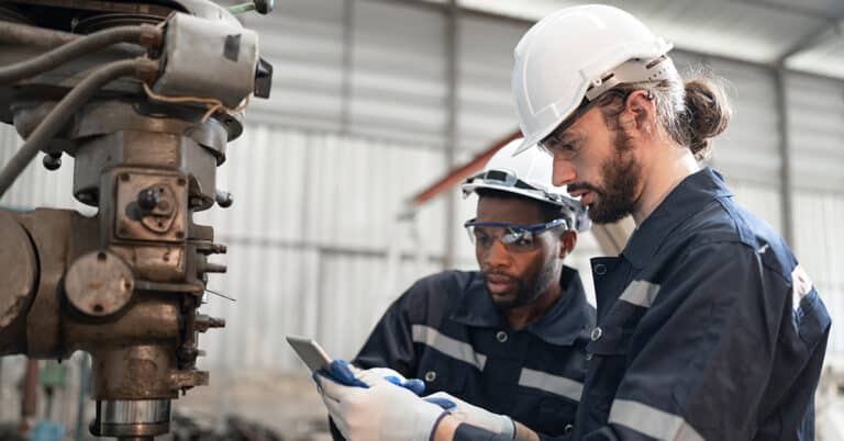 Two male engineers checking a lathe machine in a factory.