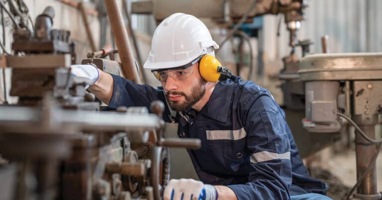 Male engineer wearing hearing protection, protective goggles, helmet and gloves while operating machinery.