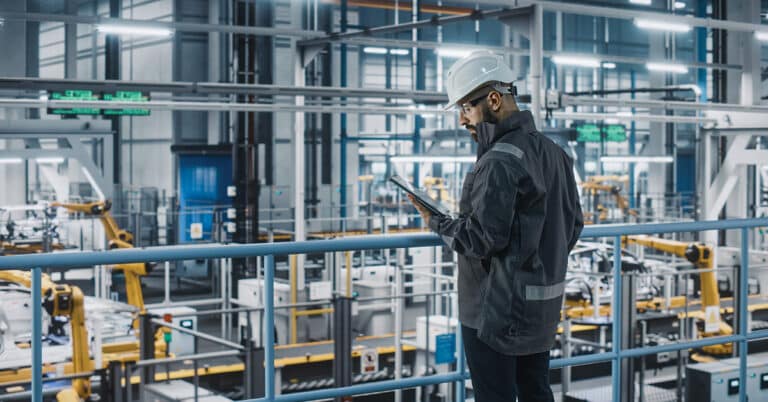 Car factory engineer overseeing production with tablet.