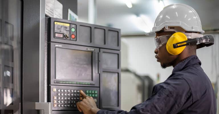 Mechanical engineer wearing safety equipment beside the automatic lathe machine in manufacturing factory.