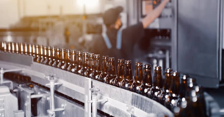 Glass beer bottles of brown color on the conveyor line of beer bottling close up.